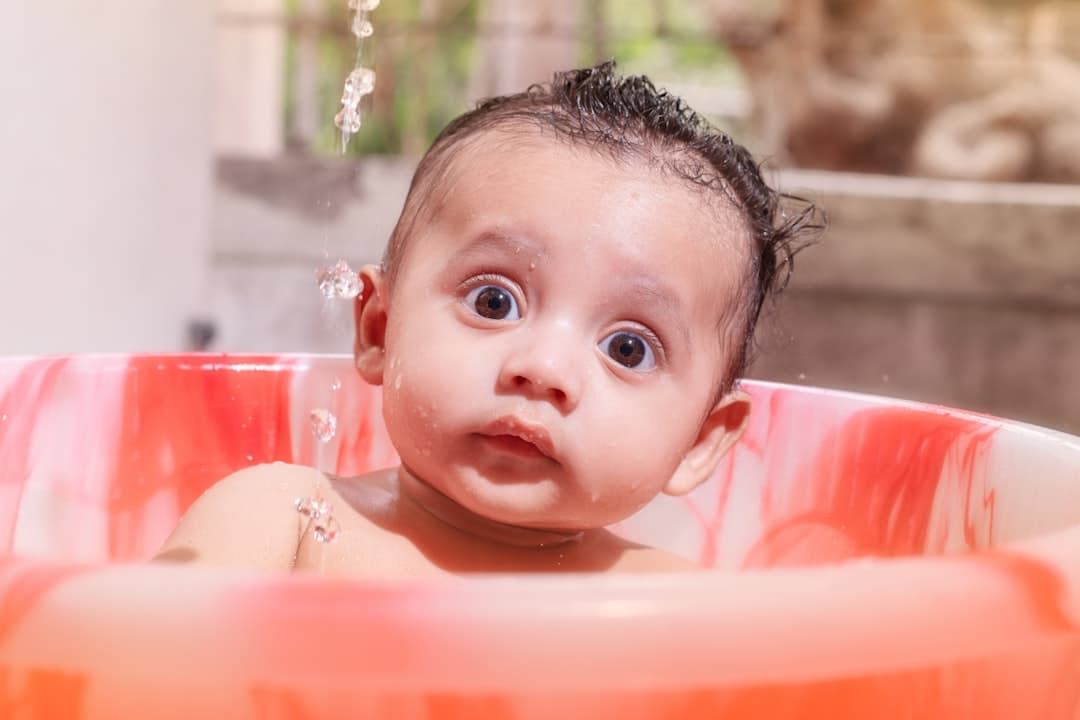 Baby with wet hair bathing in a red tub