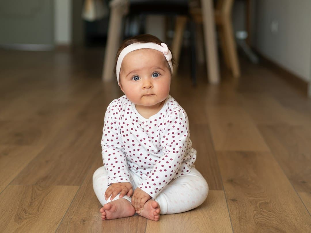 baby in white and black onesie lying on brown wooden floor
