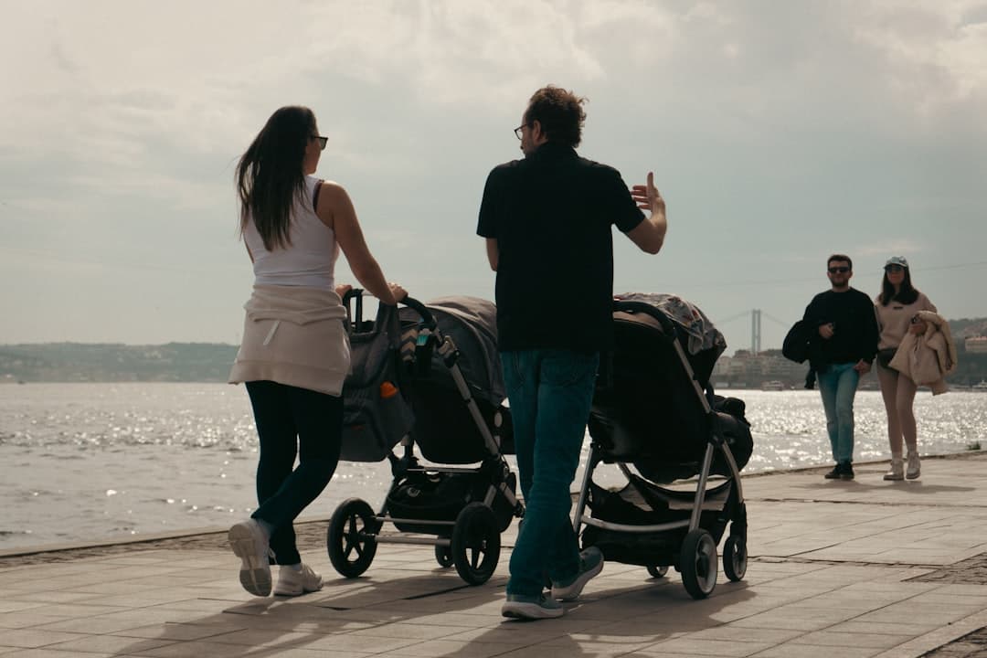 Parents stroll with double strollers by the water.