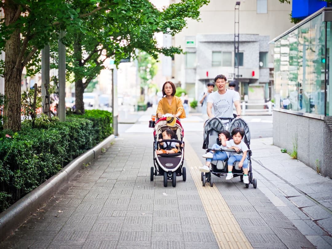 Parents pushing children in strollers on sidewalk.
