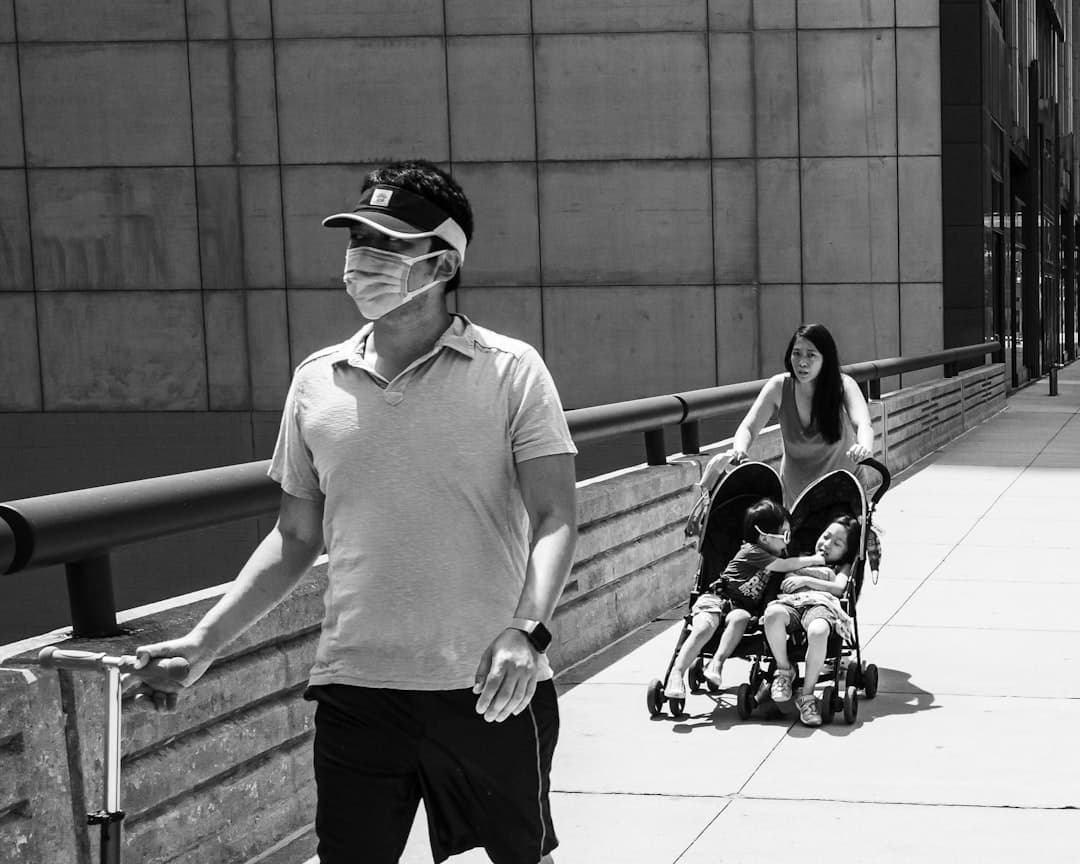 Man in mask pushes stroller with children on sidewalk