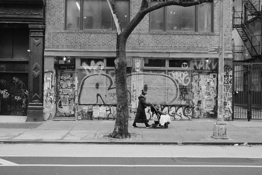 Person pushing stroller on sidewalk with graffiti wall